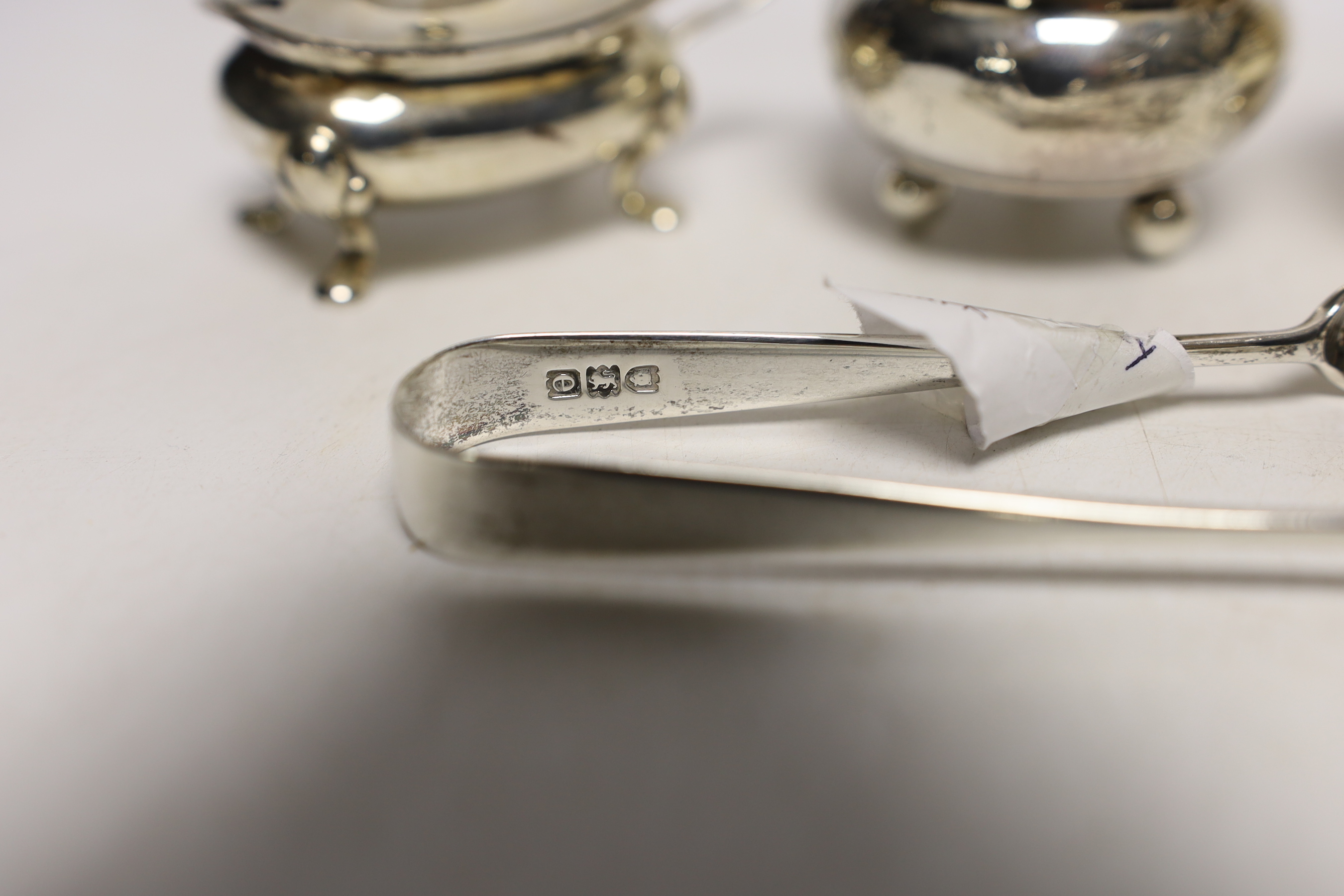 A pair of silver mustard pots, a pair of silver salts, one other silver salt, and two pairs of sugar tongs.